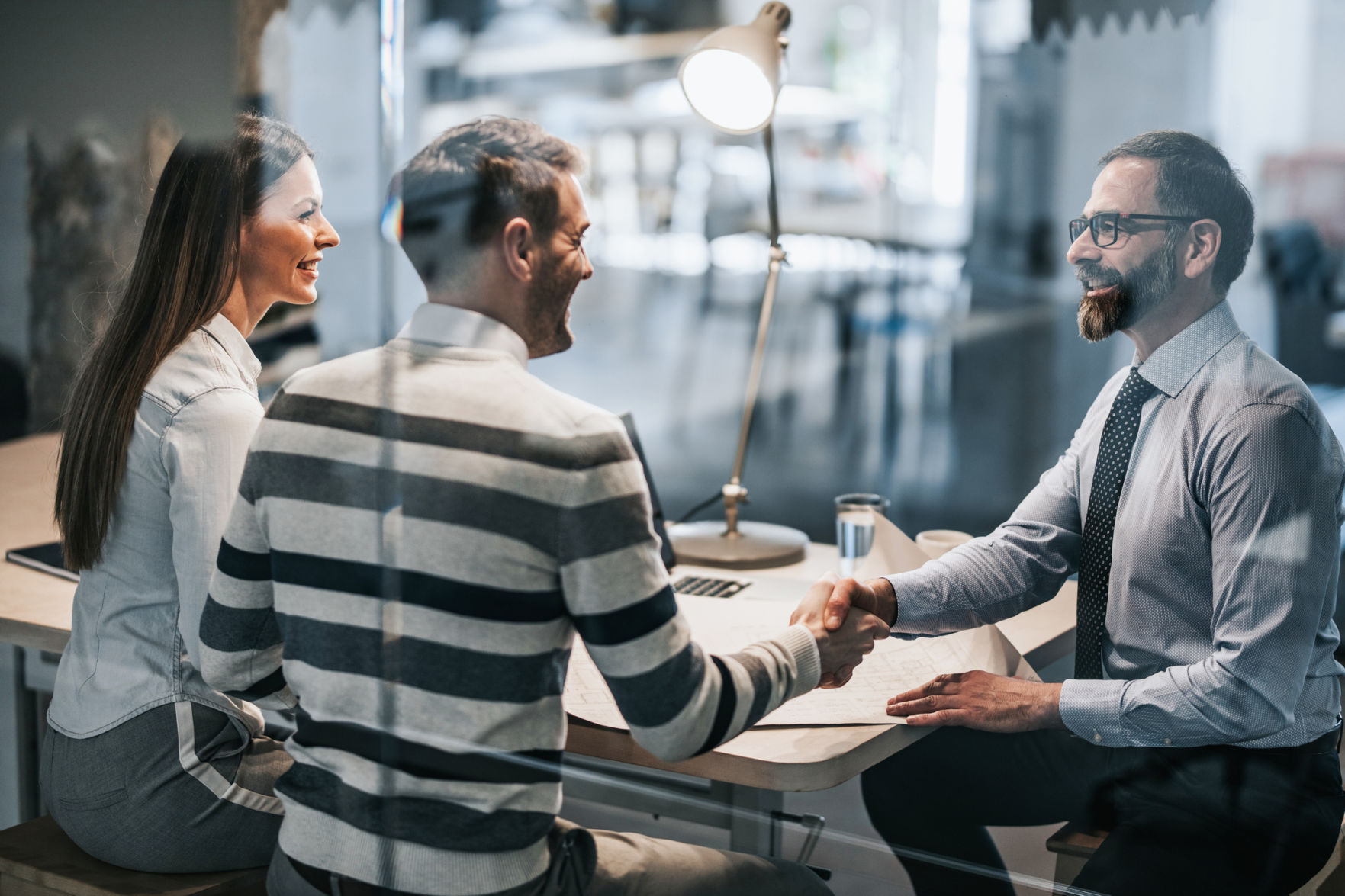 Happy couple shaking hands with real estate agent in the office.
